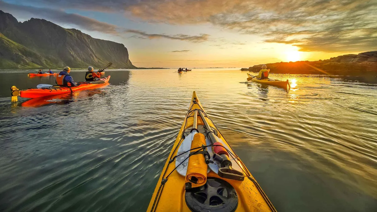 Sea kayakers paddling under the midnight sun off Eggum beach on a Lofoten Islands kayak tour in Vestvågøy, Norway